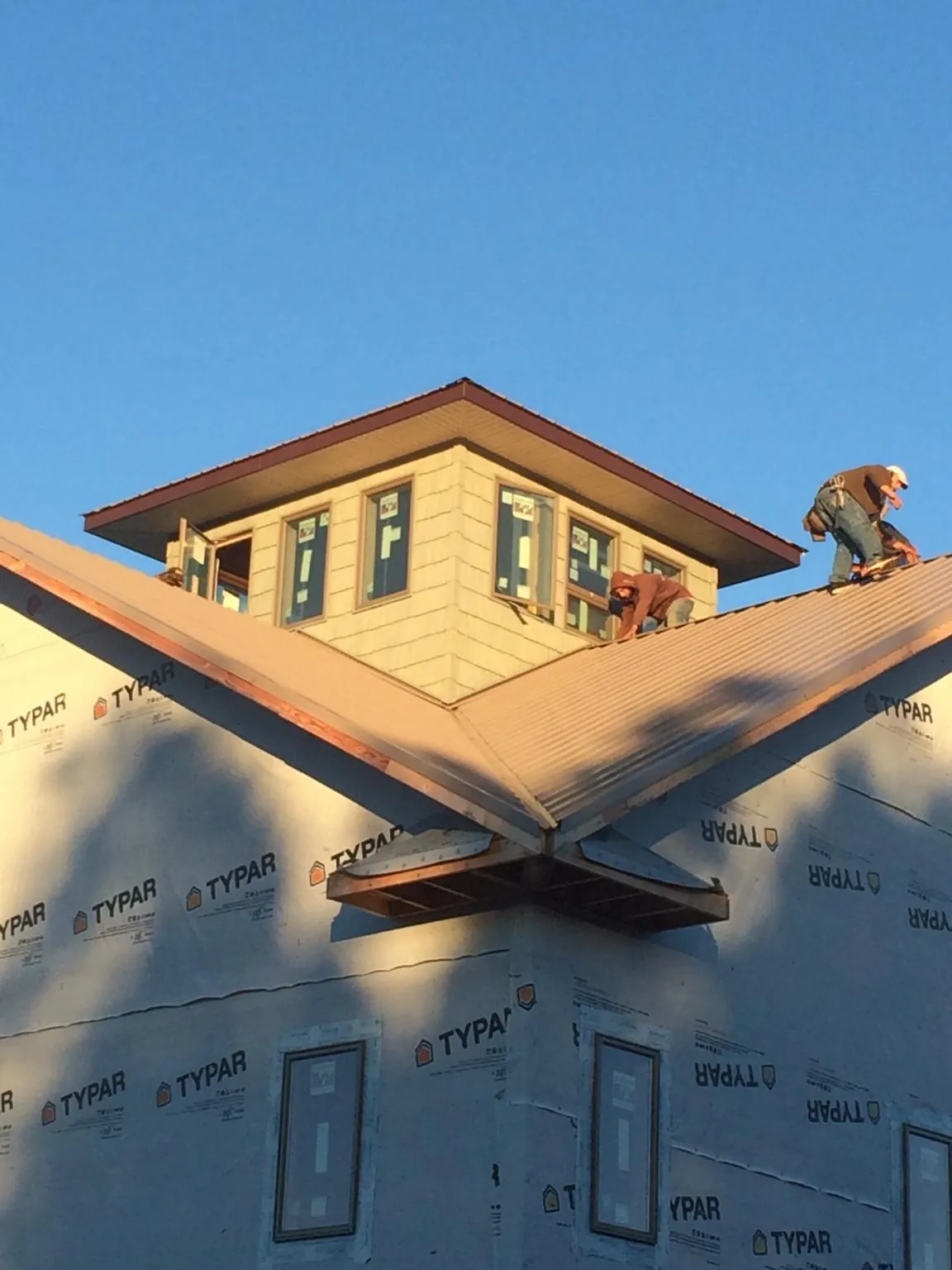 Roofers working around a rooftop cupola on a new metal roof at sunset — Roof Waterproofing in Riverside by Roofing Brothers